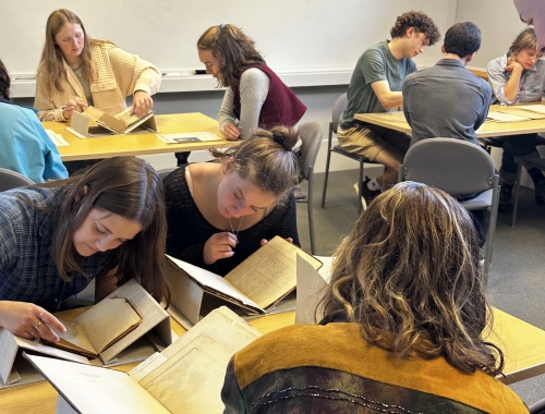 Students grouped around tables leaning over old manuscripts and books.