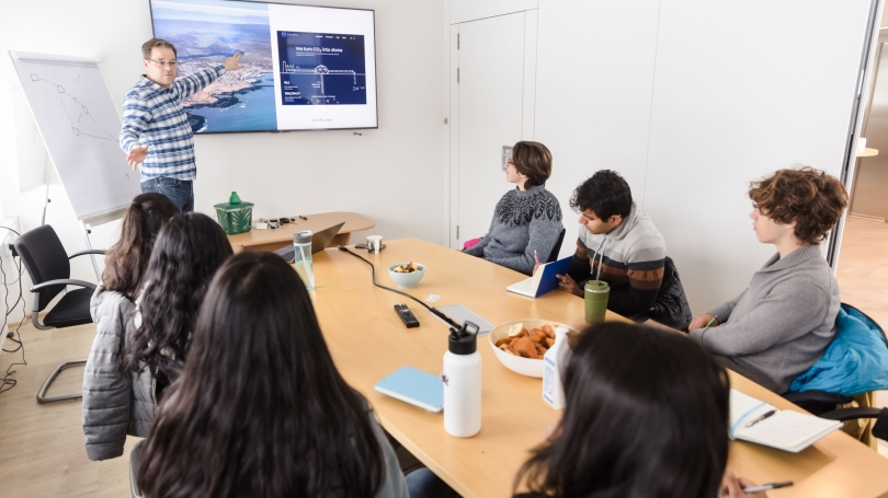 A man pointing at a slideshow while speaking to students