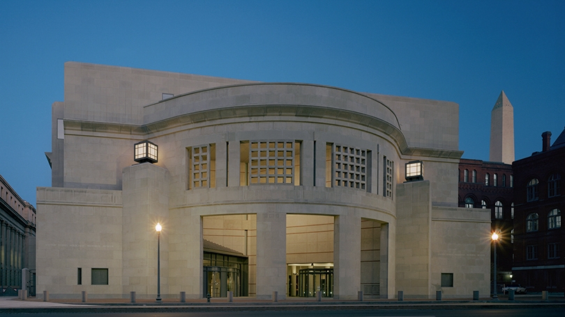 the exterior of the Holocaust Museum at night with the Washington Monument in the background